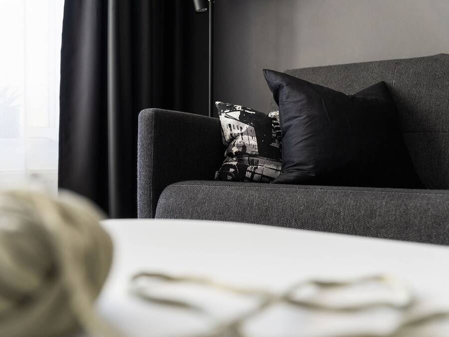 Una sala de estar moderna con un sofá gris, una almohada negra y una mesa blanca con un ovillo de lana y un par de gafas.