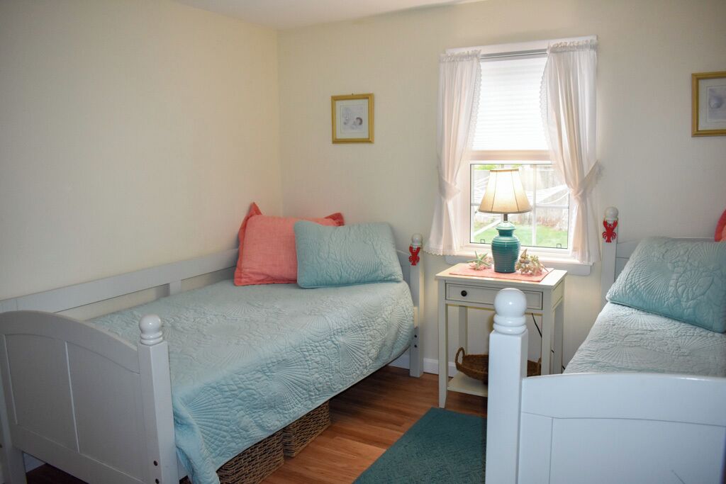 Un dormitorio con dos camas individuales, una mesita de noche pequeña con una lámpara y una ventana con cortinas.