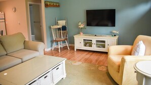 Een woonkamer met een bank, fauteuil en een aan de muur bevestigde televisie.