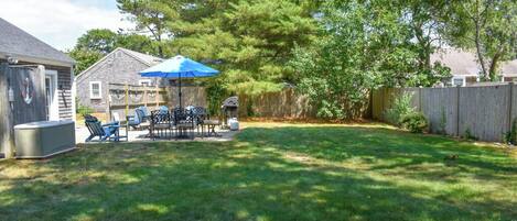 A backyard with a patio table and chairs, a barbecue grill, and a blue umbrella.