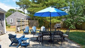 Een terras met een tafel, stoelen, een blauwe parasol en een barbecue.