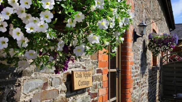 Una casetta con un muro in pietra e un cartello con su scritto 'Oak Apple Cottage'.