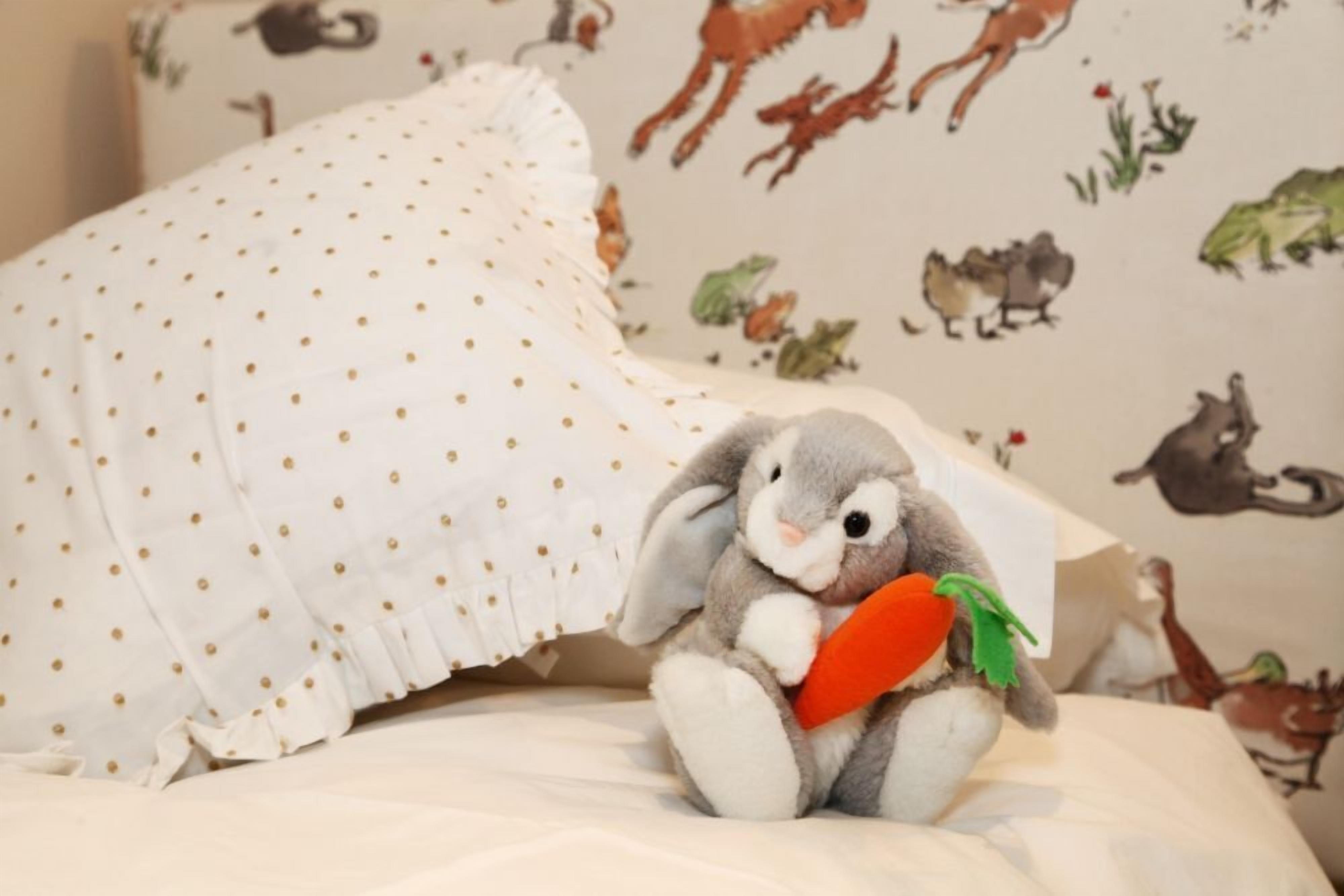 A bed with a polka-dotted pillow and a stuffed rabbit toy holding a carrot.