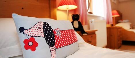 Een bed met een kussen waarop een hond is afgebeeld, een rode lamp, een teddybeer en een houten hoofdeinde.