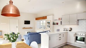 Una cucina moderna con mobili bianchi, forno integrato e lampada a sospensione in rame.