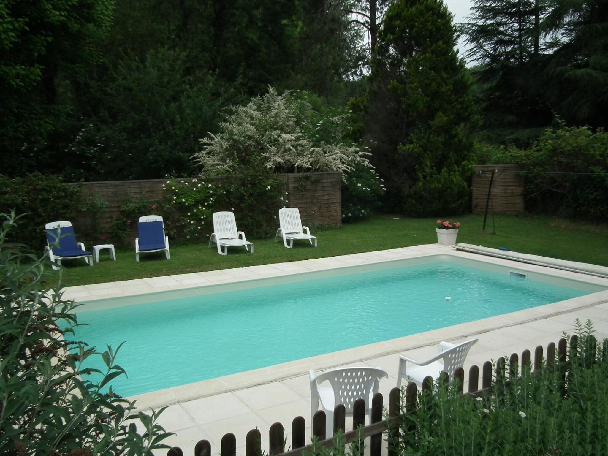 A rectangular swimming pool with a tiled deck, surrounded by a wooden fence.