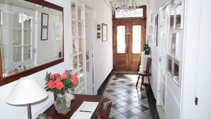 Un pasillo con puerta de madera, un candelabro, una mesa con un florero y un espejo.