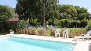 Piscina rectangular con borde de baldosas, rodeada por un cerco de madera y abundante vegetación.