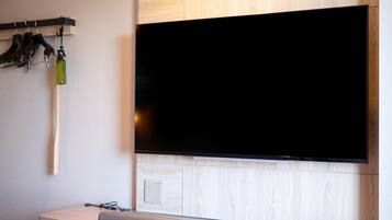 A modern room with a large flat-screen TV mounted on a wooden wall, a desk with a chair, and a coat rack with hanging items.