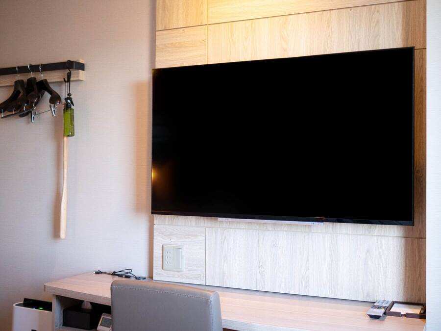 A modern room with a large flat-screen TV mounted on a wooden wall, a desk with a chair, and a coat rack with hanging items.