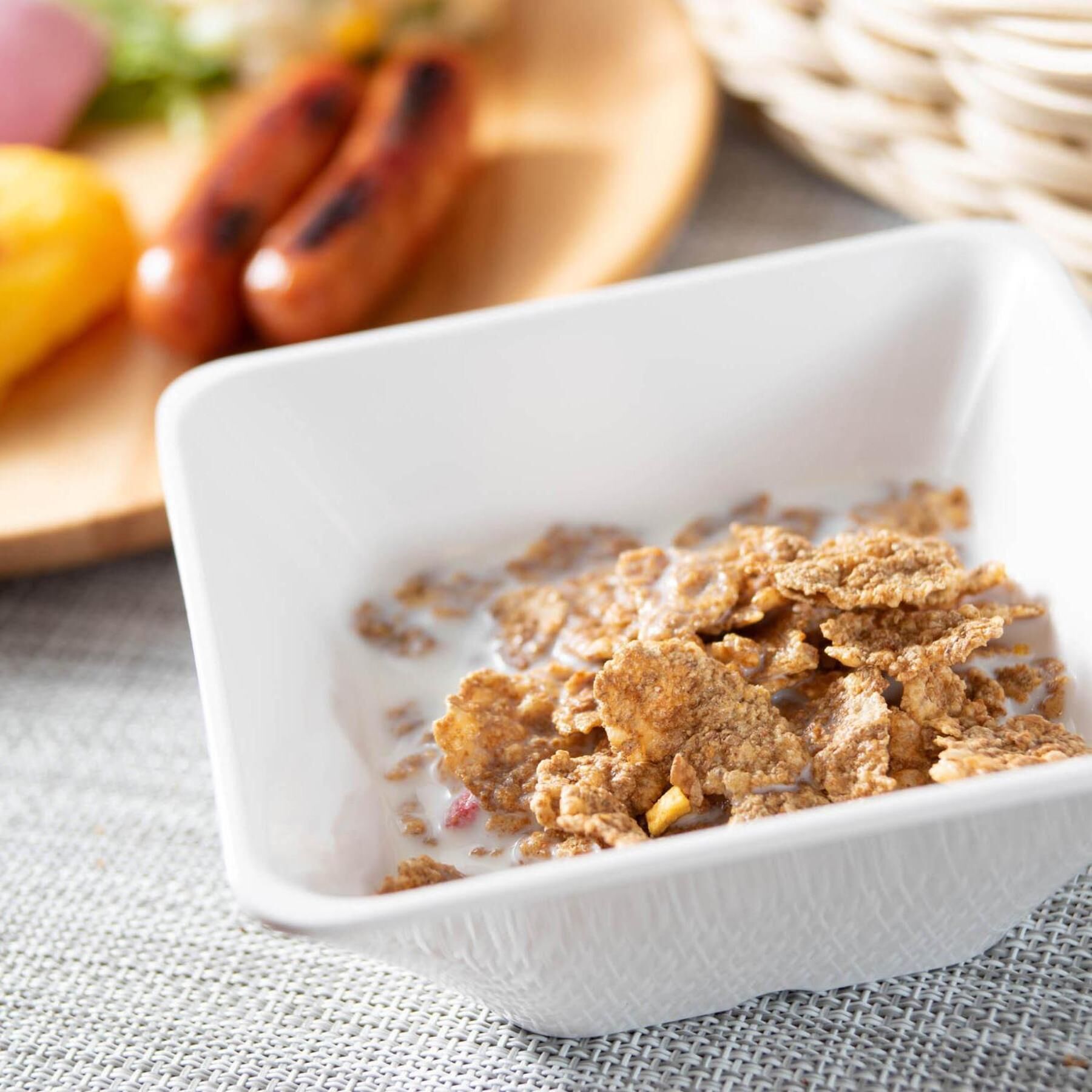 Un tazón blanco con textura que contiene un alimento, posiblemente cereal o granola, sobre un tapete tejido.