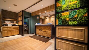 A hotel reception area with a wooden reception desk, a digital display, and a wall-mounted plant display.