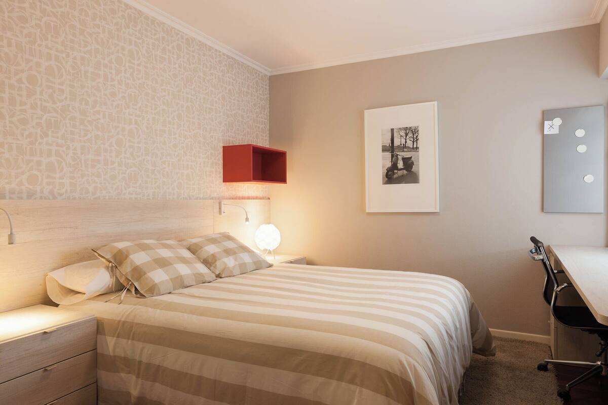 Een slaapkamer met een bed, nachtkastje, bureau en stoel.