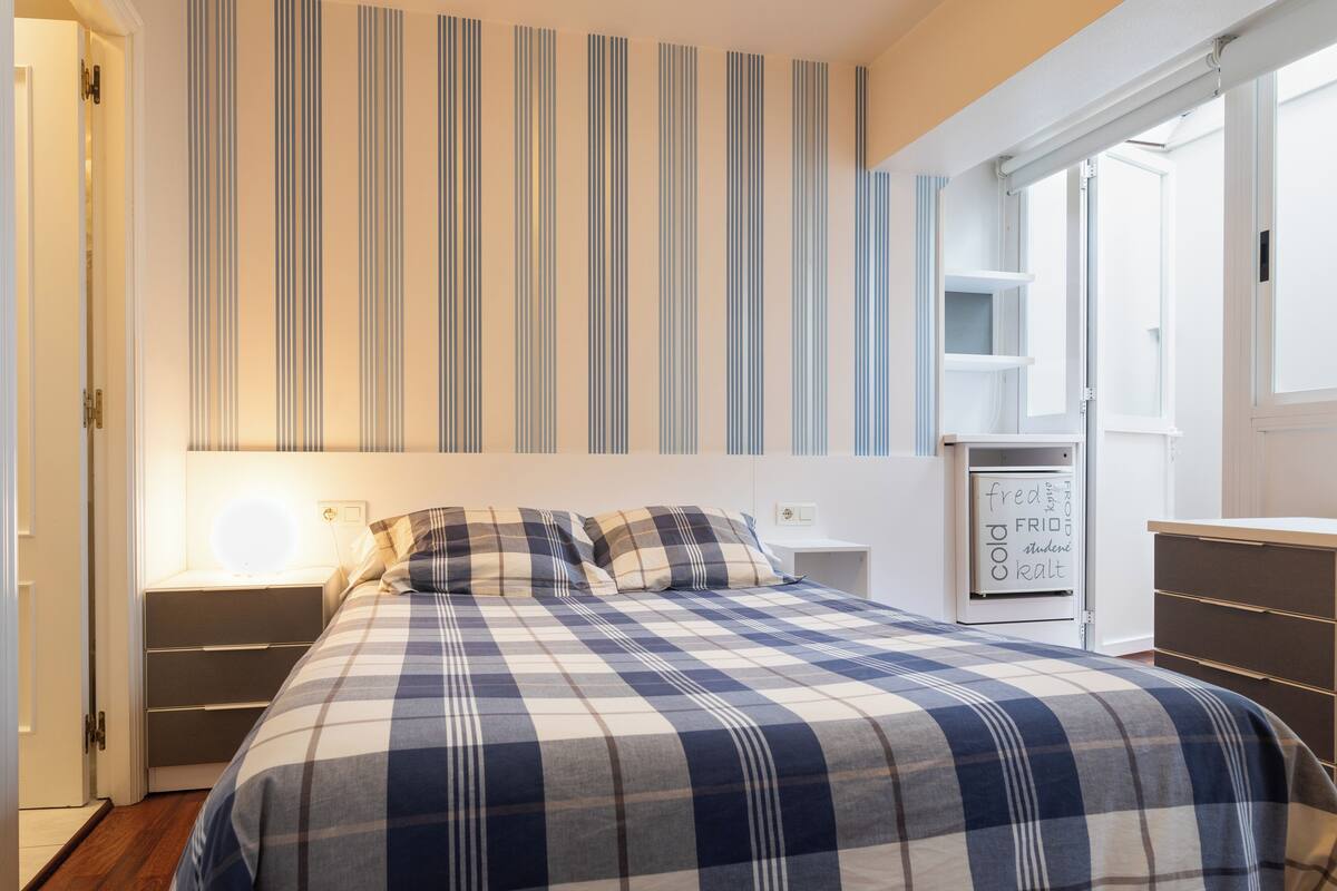 Een slaapkamer met een geruit bedovertrek, een nachtkastje met een lamp en een kledingkast.