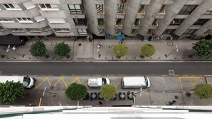 Luchtbeeld van een meerlaags gebouw met een opvallende, hoekige architectuur, voorzien van balkons met beplanting en een straat met geparkeerde voertuigen en voetgangers.