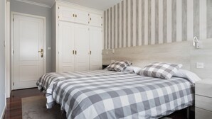 Een slaapkamer met een tweepersoonsbed, een nachtkastje, een garderobe en een gestreepte wand.