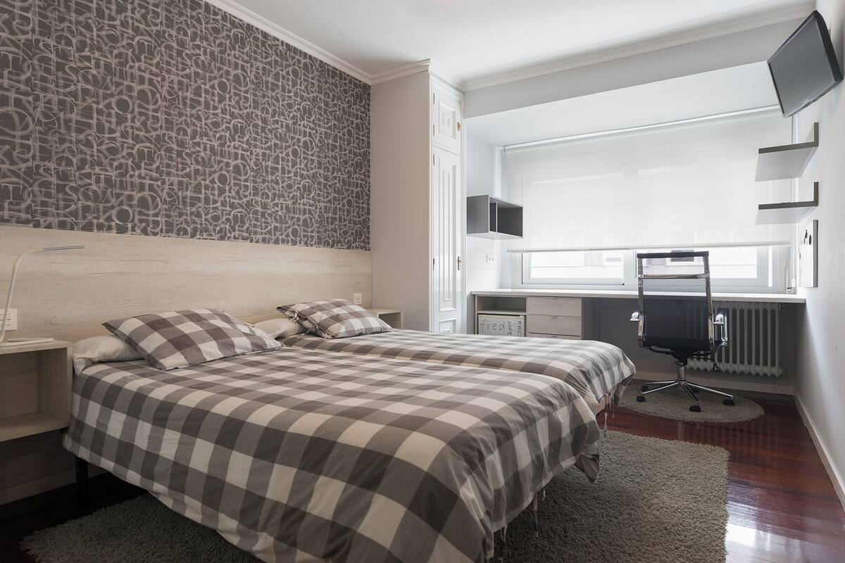 Een slaapkamer met een bed, een bureau, een stoel, een televisie en een radiator.
