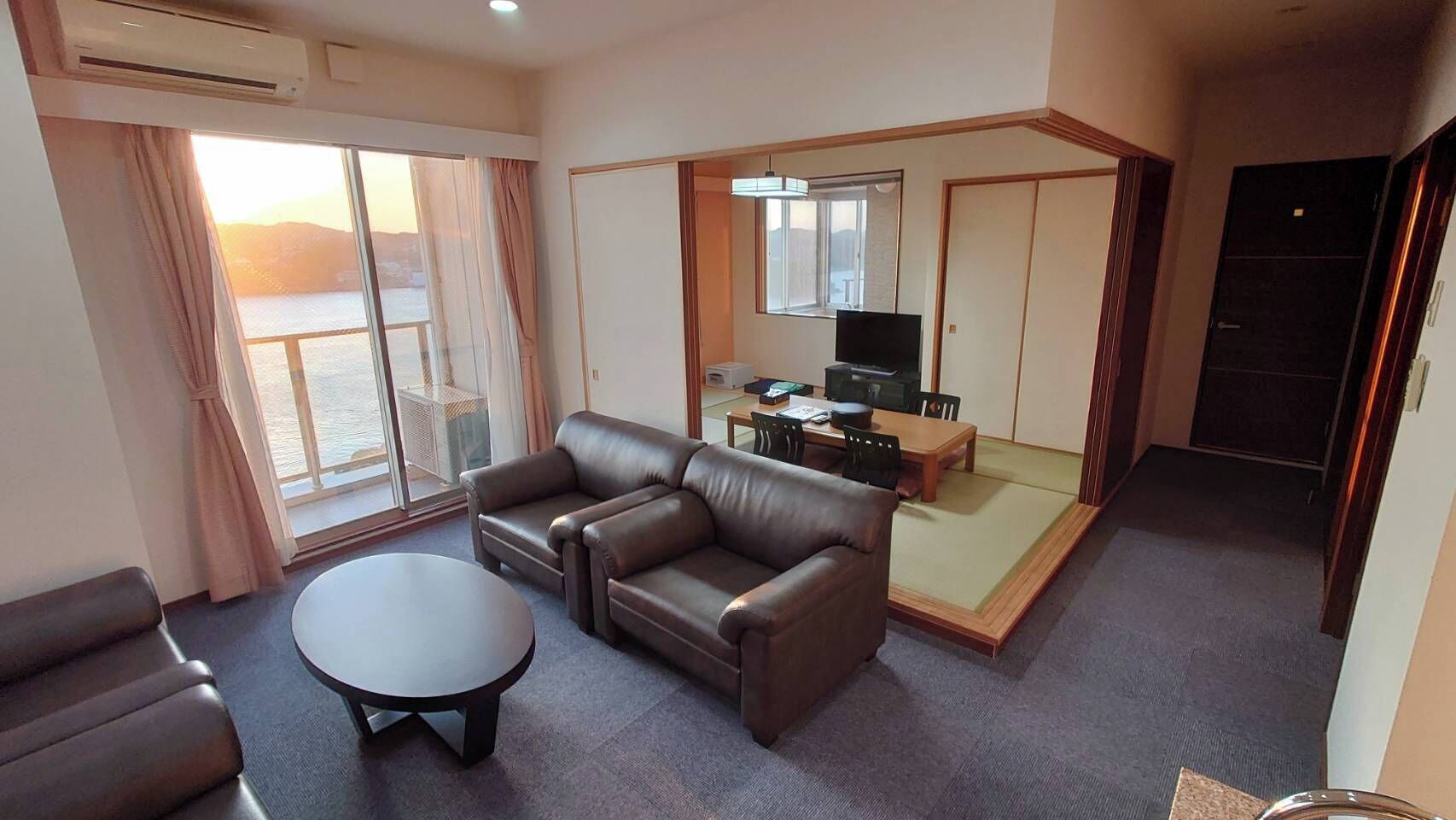 Habitación de hotel con sofá, una mesita, televisor y puerta corredera que da a un balcón.