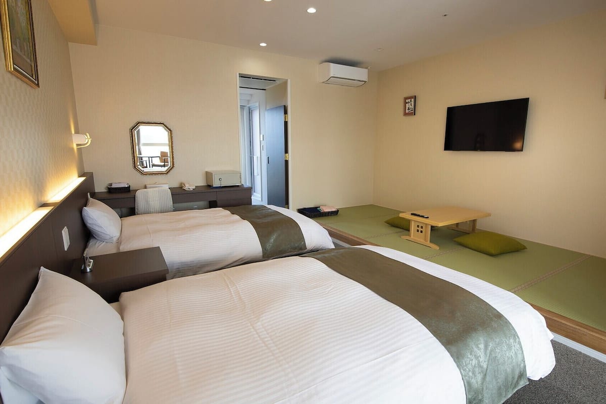 Una habitación de hotel con dos camas, un escritorio, una silla, un televisor y una mesita.