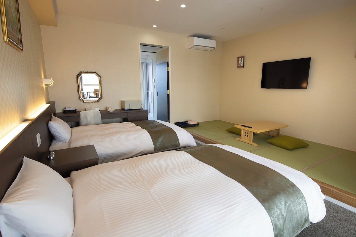 A hotel room with two beds, a desk, a chair, a television, and a small table.