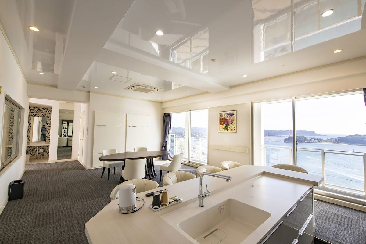 Habitación de hotel moderna con un ventanal grande que ofrece vistas panorámicas, una kitchenette, un comedor y un baño.