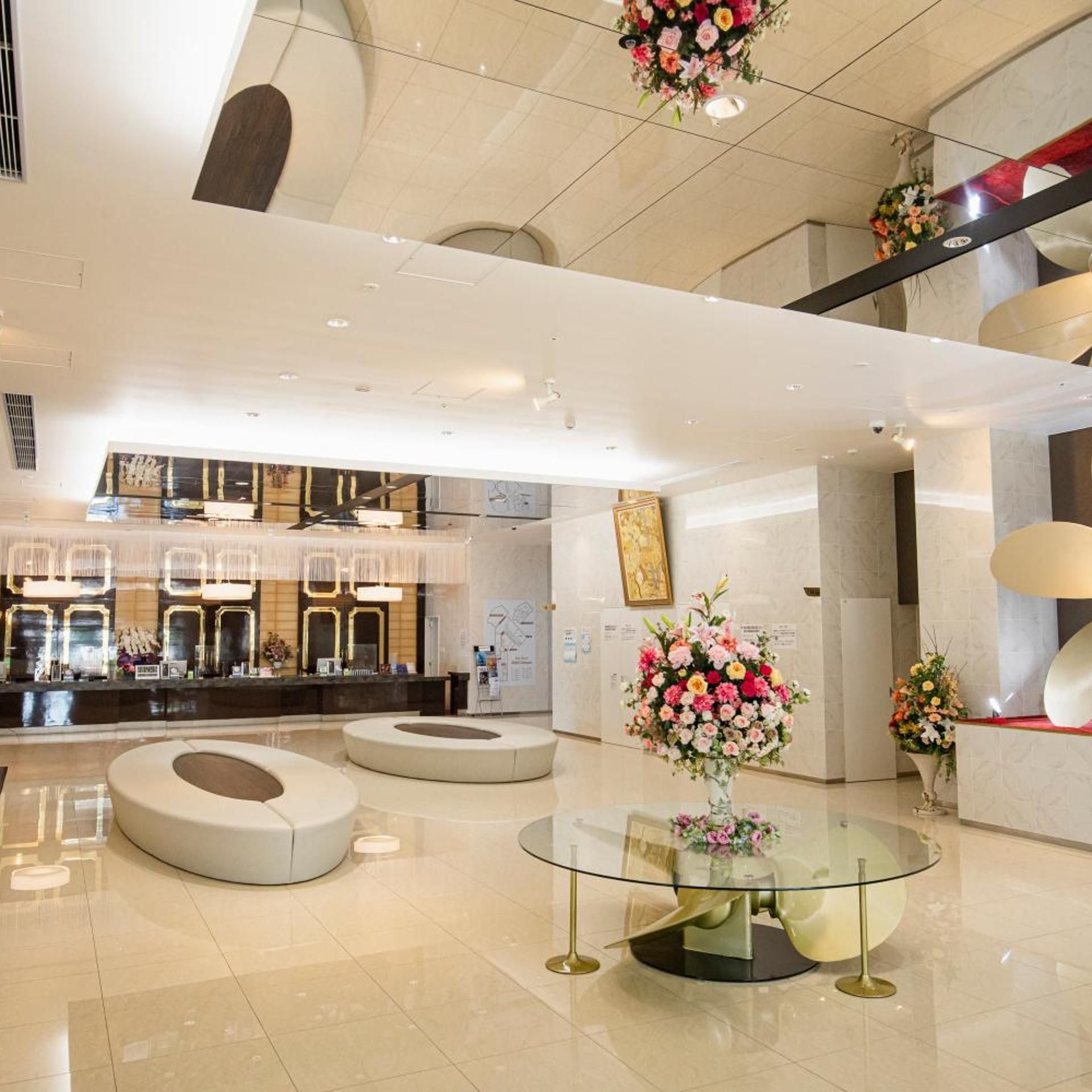 A modern hotel lobby with a reception desk, seating areas, and a glass table with a floral centerpiece.
