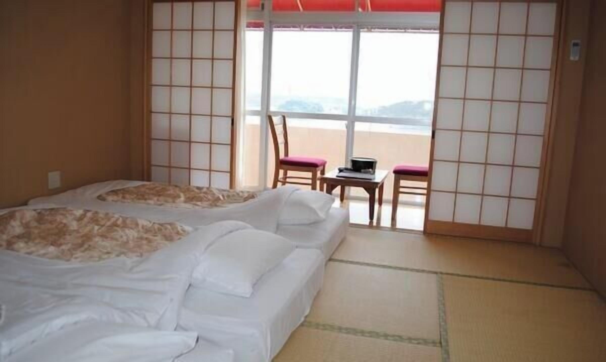 Habitación de hotel con dos camas, una mesita, sillas y vistas al mar.