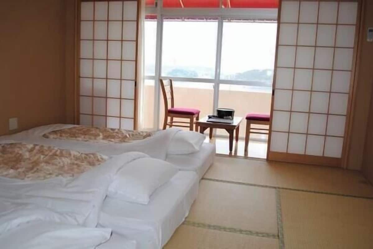 Habitación de hotel con dos camas, una mesita, sillas y vistas al mar.