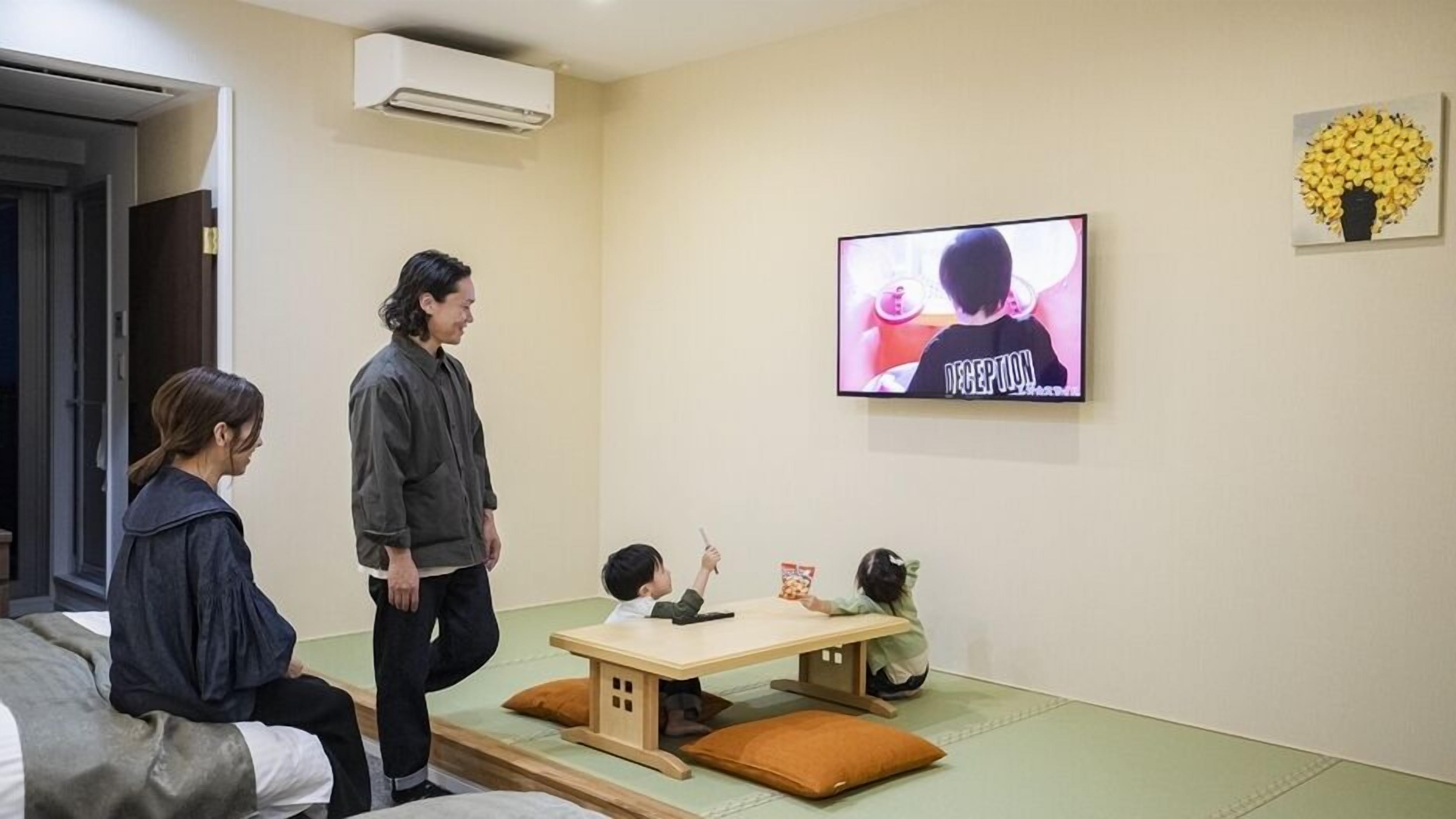 A room with a TV, a sofa, a table, and a wall-mounted air conditioner.