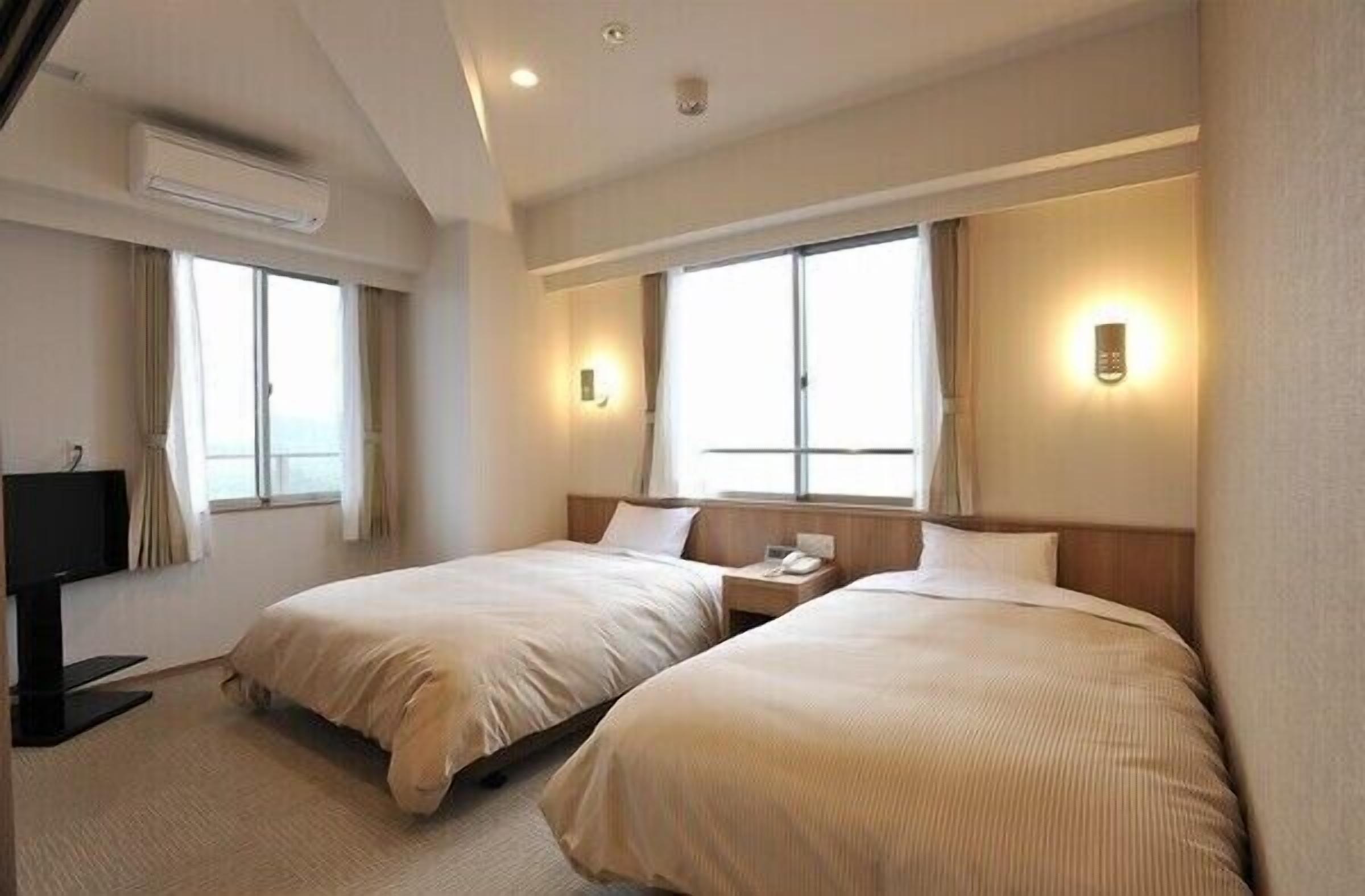 A hotel room with two beds, a TV, and a window.