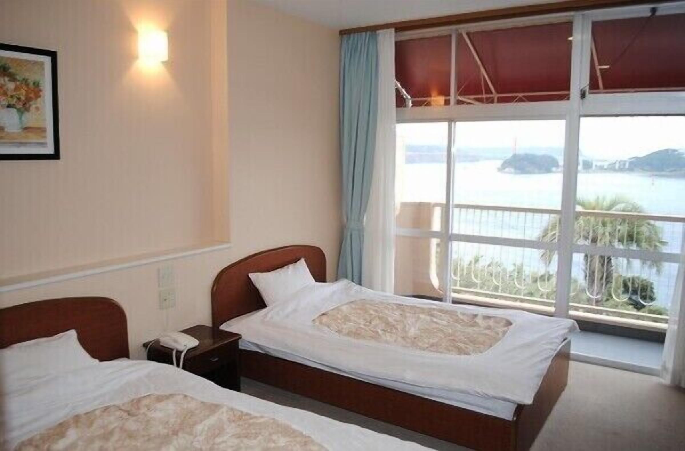 Habitación de hotel con dos camas, un amplio ventanal con vista al mar, un cuadro en la pared y una lámpara de noche.