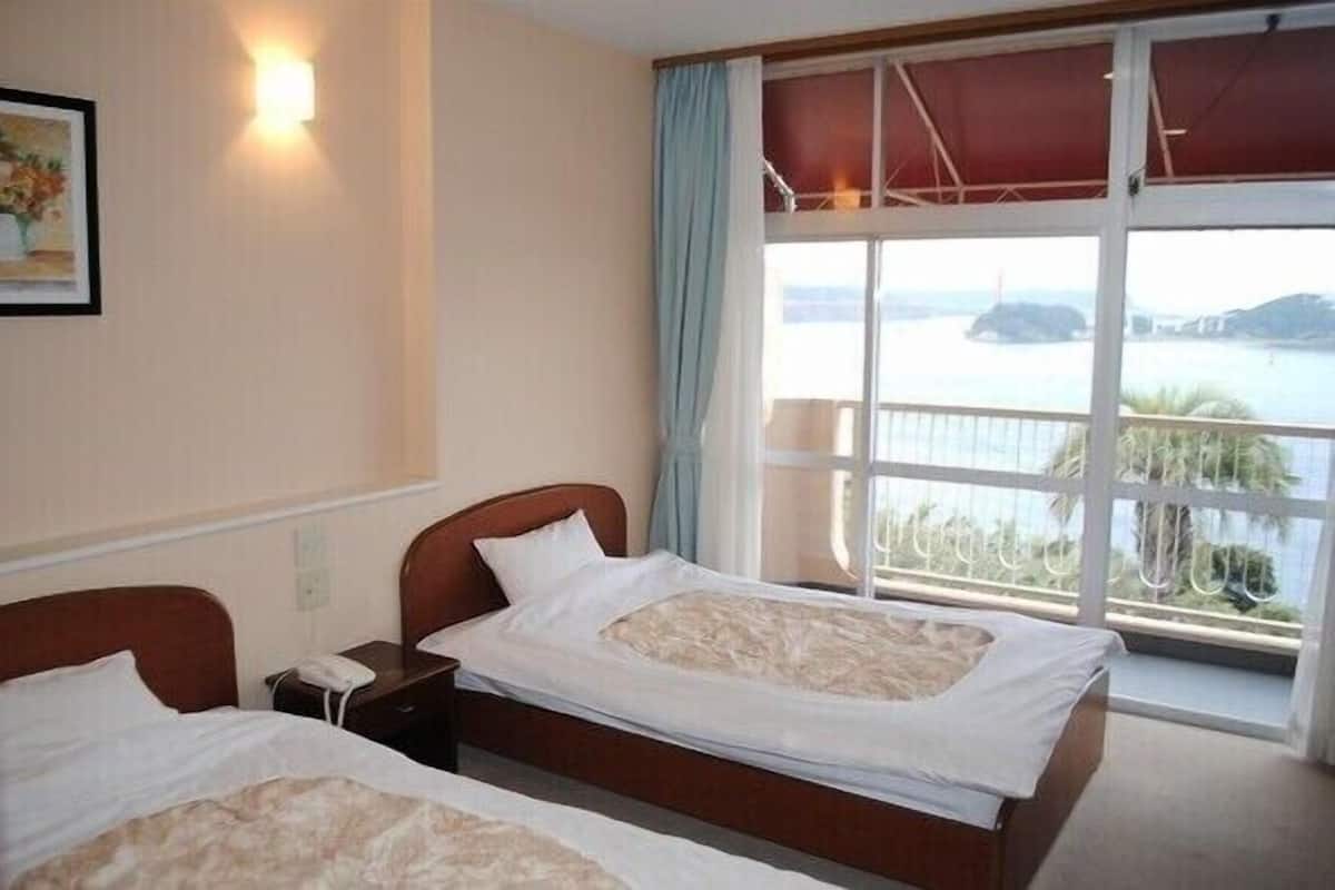 Habitación de hotel con dos camas, un amplio ventanal con vista al mar, un cuadro en la pared y una lámpara de noche.