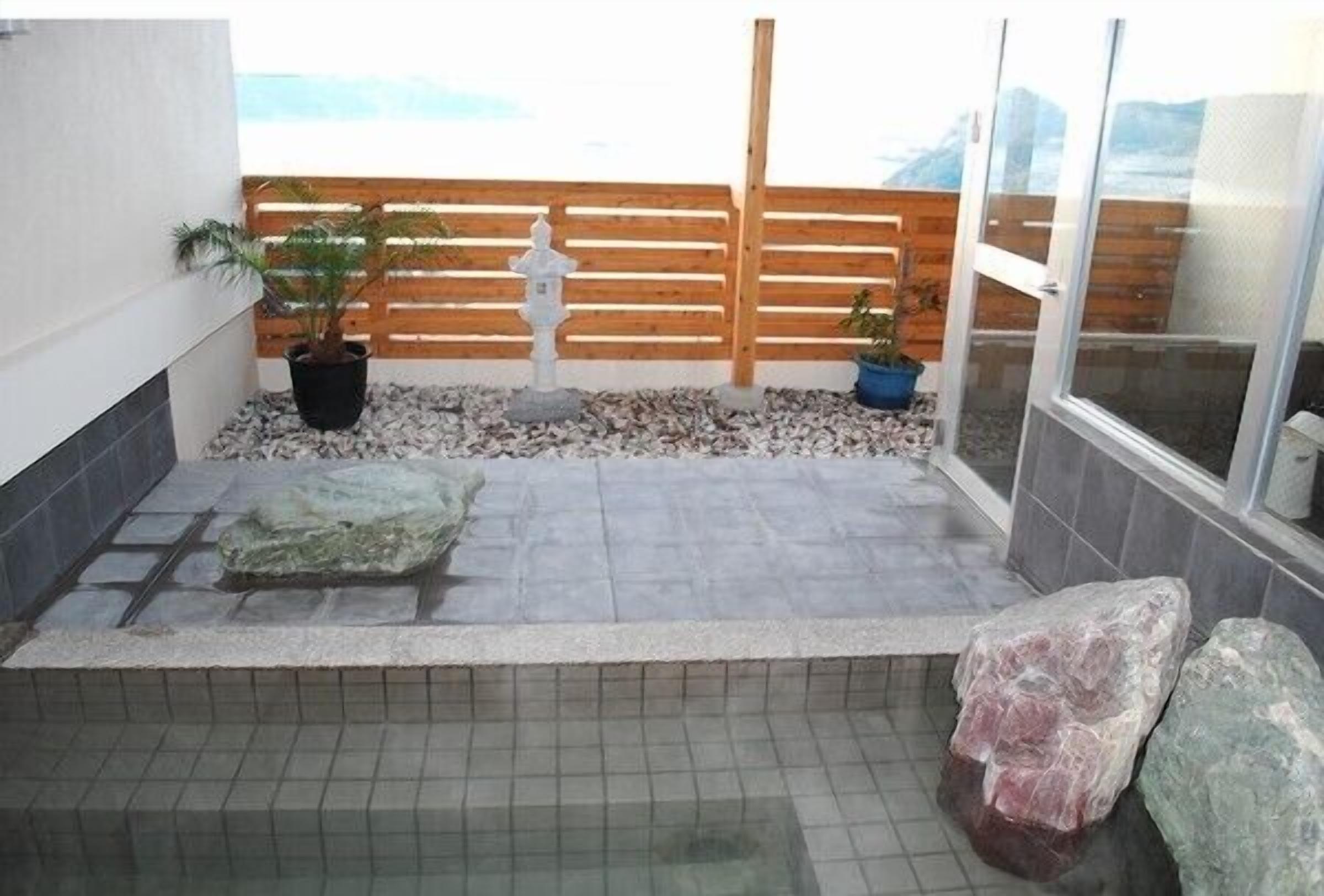 Un pequeño espacio al aire libre con un banco de piedra, plantas en macetas y una valla de madera.