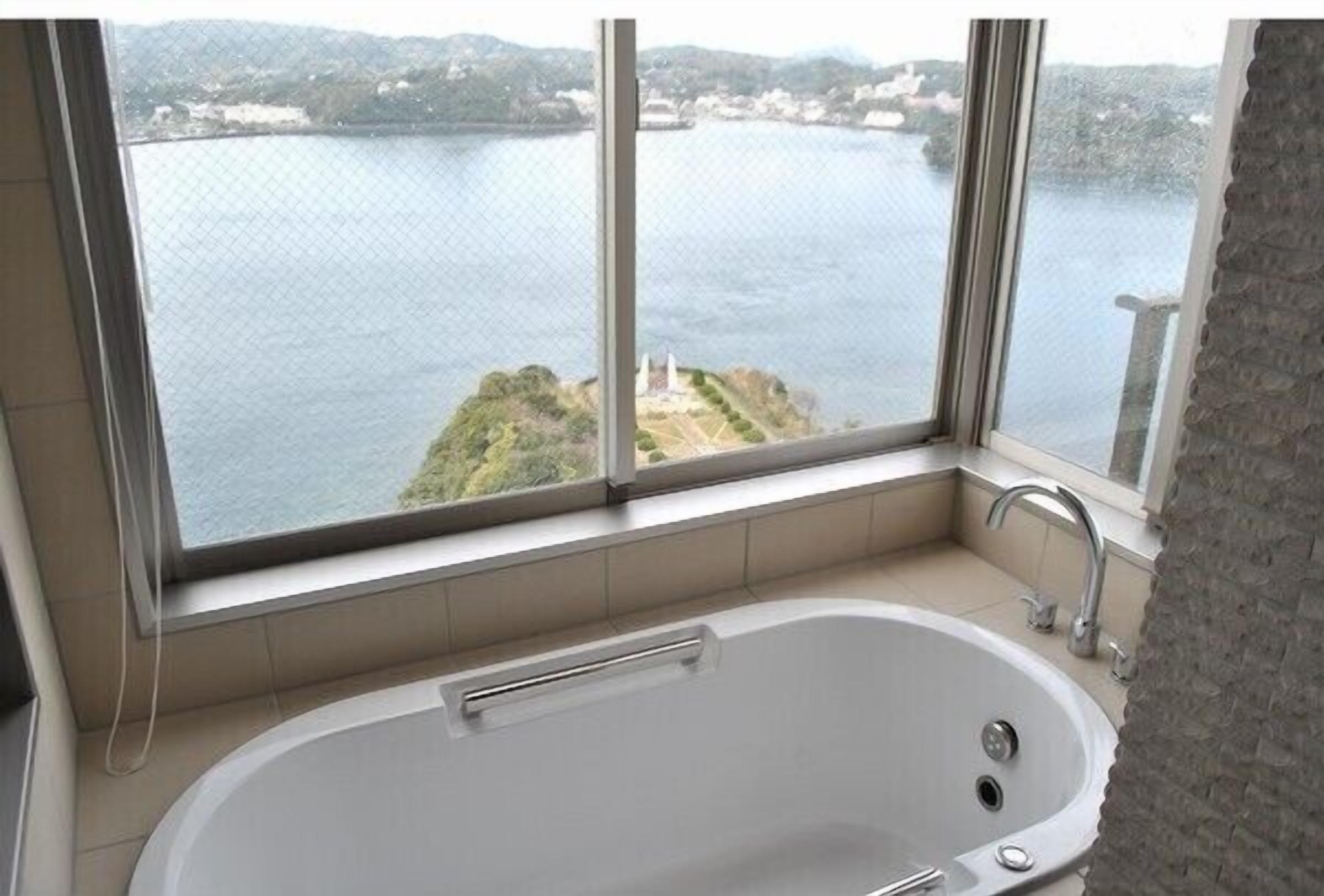 A bathroom with a bathtub, a window, and a view of a body of water and a distant island.