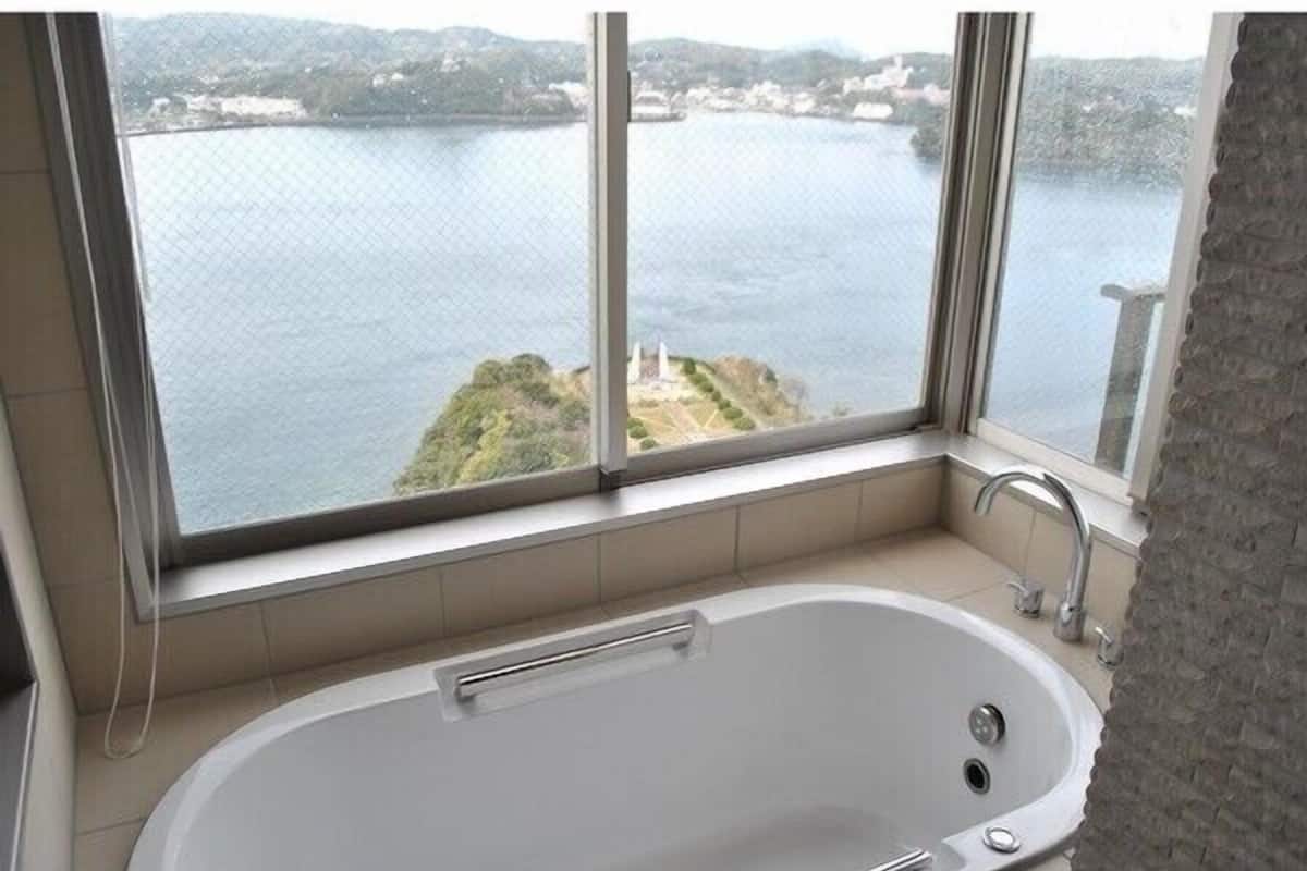 Un baño con bañera, ventana y vista a un cuerpo de agua y una isla distante.