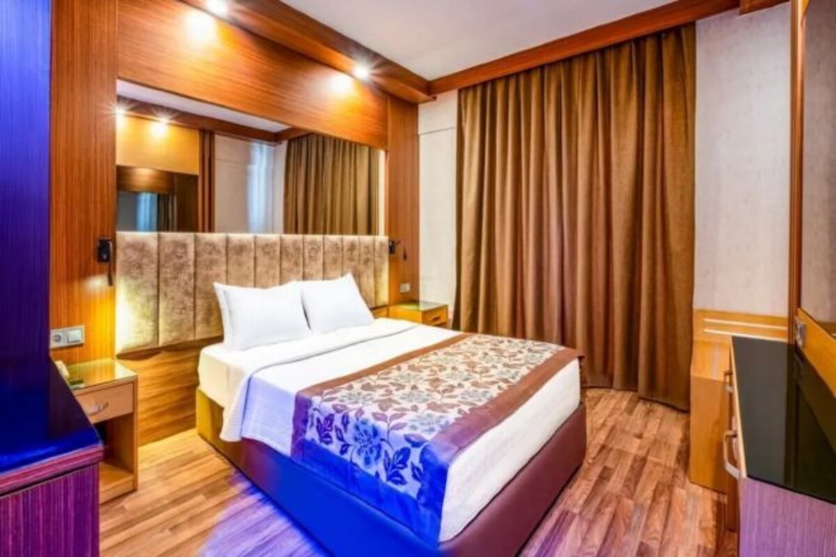 Une chambre d’hôtel avec une tête de lit en bois, un lit recouvert d’une couvre-lit à motifs floraux, une table de chevet et une armoire.