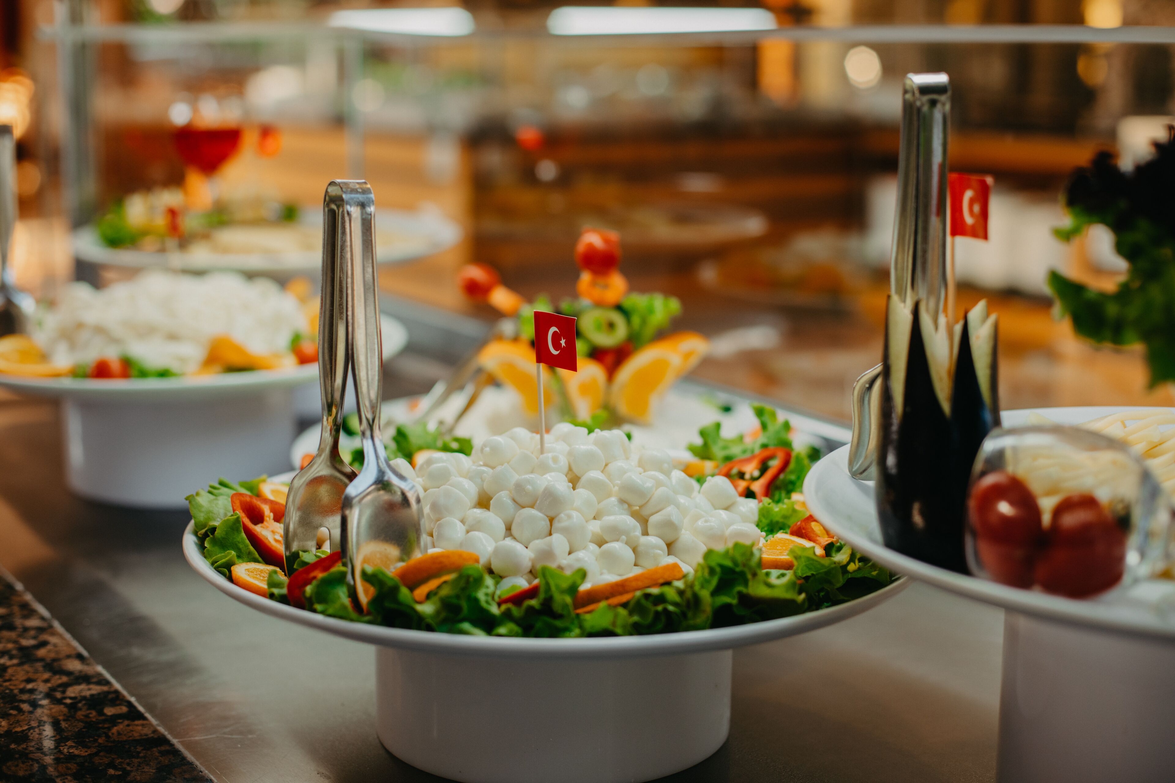 Buffet com diversos pratos, incluindo saladas e uma tigela com esferas brancas, provavelmente queijo ou algo parecido.