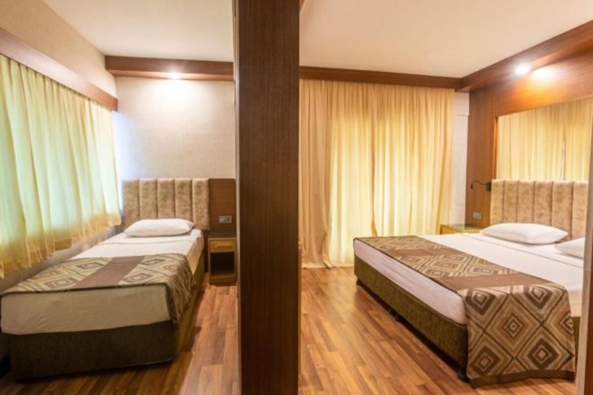 Une chambre d’hôtel avec deux lits simples, un plancher en bois et des rideaux de couleur beige.