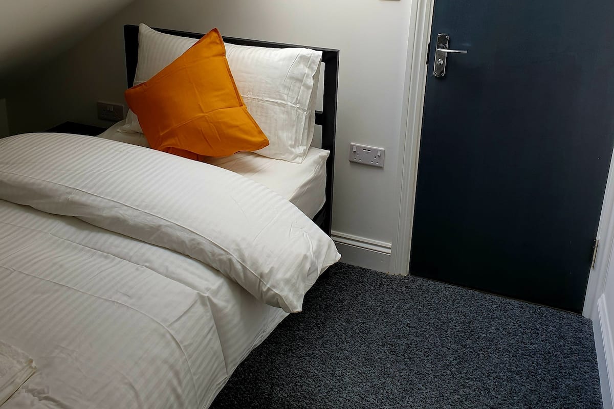 A bedroom with a bed, a nightstand, a door, and a skylight.