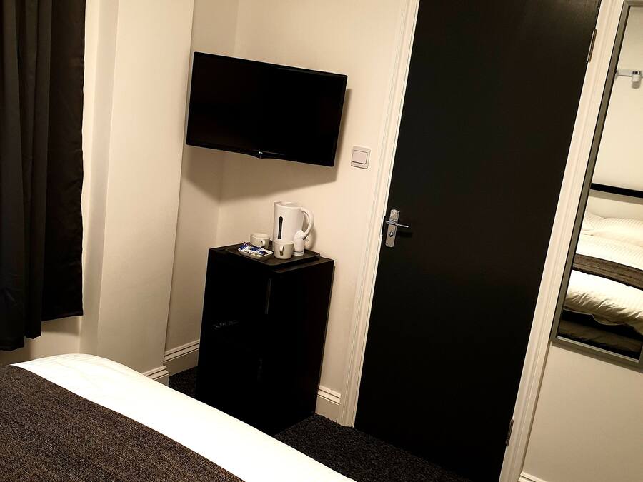 A hotel room with a bed, a flat-screen TV mounted on the wall, a small table with a coffee maker, and a door with a window.