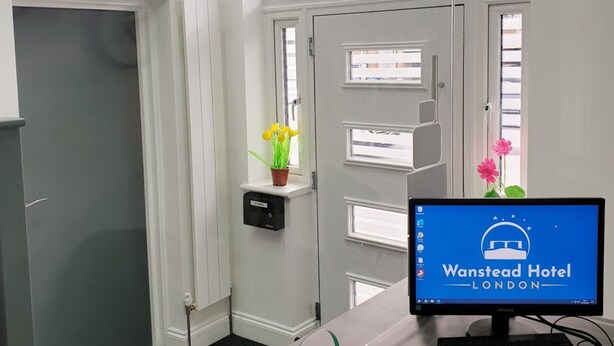 Un espace d’accueil avec un écran affichant la mention « Hôtel Wanstead, Londres », un comptoir de réception, une porte avec une fenêtre et une petite plante posée sur le rebord de la fenêtre.