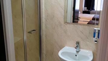 Un baño con cabina de ducha de vidrio, lavamanos pedestal y espejo sobre el lavamanos.