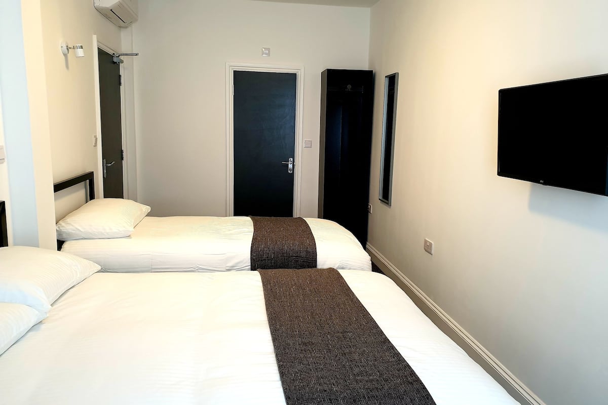 A hotel room with two beds, a TV mounted on the wall, and a door leading to another room.