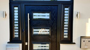 Une porte d’entrée noire, avec une plaque indiquant « 2B LONSDALE ROAD » au-dessus. De part et d’autre de la porte, on trouve deux boîtes aux lettres et, sur le côté droit, un système d’interphone fixé au mur.
