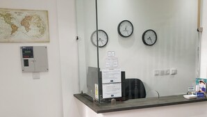 Un espace d’accueil doté d’une cloison en verre, de deux horloges, d’une carte, d’une balance et d’une chaise.