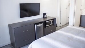 Et hotelværelse med en seng, et fjernsyn ophængt på væggen, kaffemaskine, mikrobølgeovn og et lille køleskab.