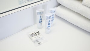 Et badeværelse med et spejl, der viser en stak hvide håndklæder og tre flasker TruLY body wash og balsam.