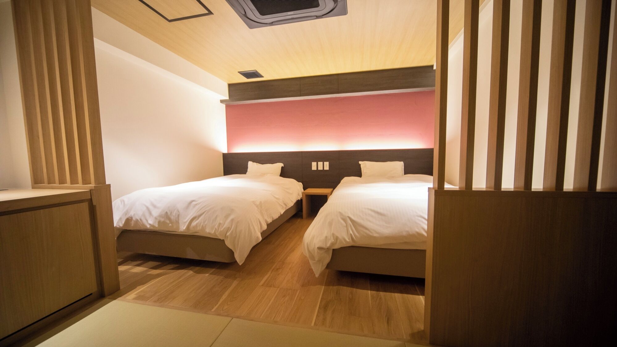 Ein Hotelzimmer mit zwei Betten, Holzboden, Deckenventilator und einer Wandleuchte.