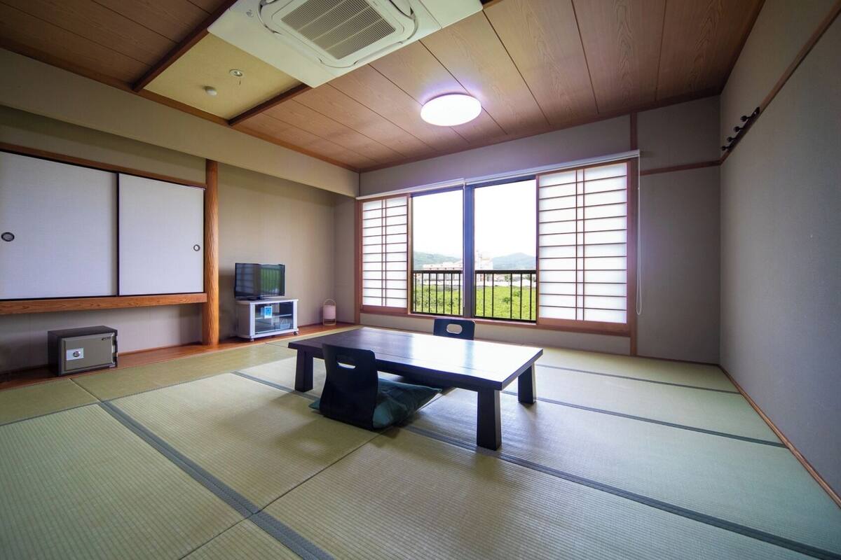 Um espaço com tatames, porta deslizante, uma televisão pequena e uma mesa.