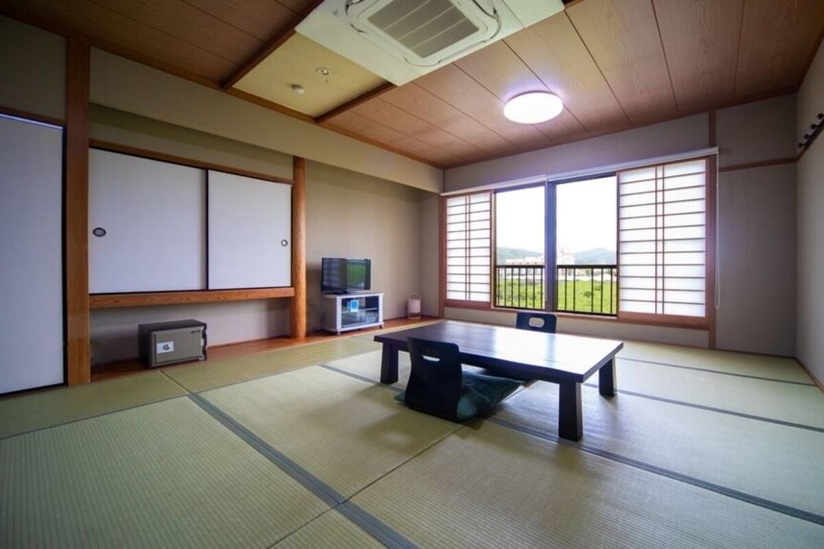Um quarto com tatames, uma mesa de tatame, uma televisão e uma porta deslizante.